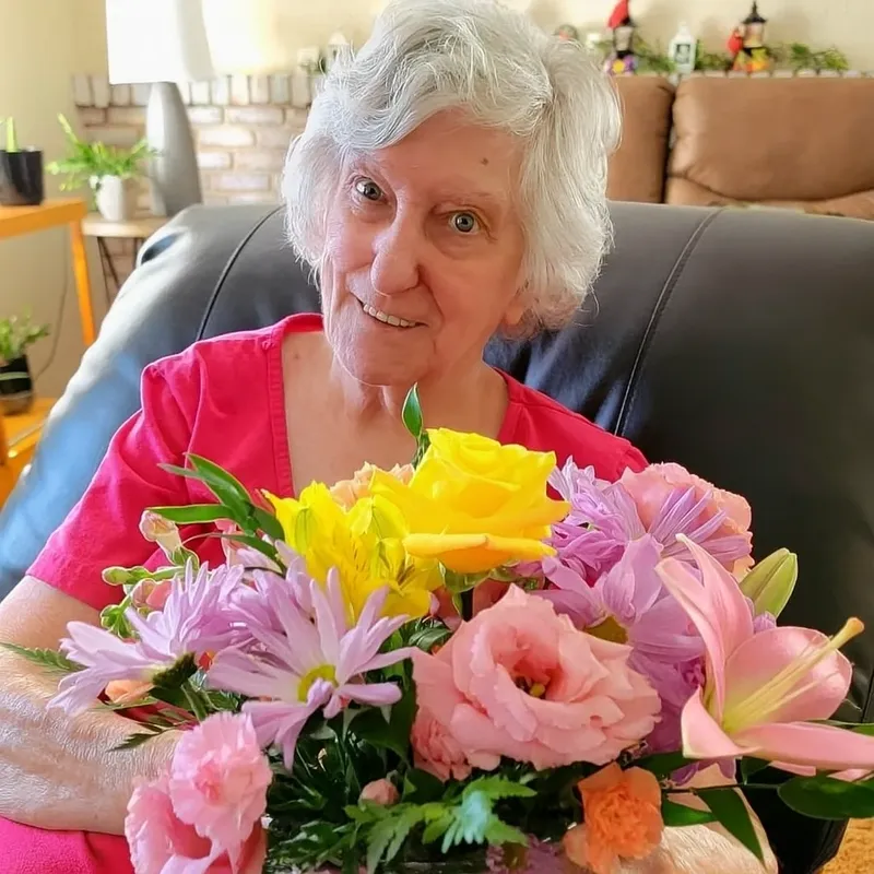 Elderly woman smiling, holding colorful flowers.